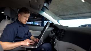 Law enforcement  officer in squad car typing on a laptop. 