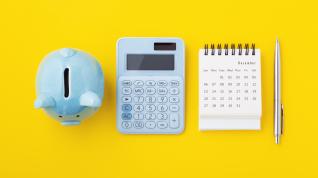 A piggy bank, calculator, calendar and pen on a yellow background. 