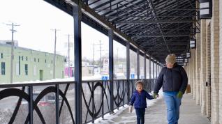 An adult and child holding hands while walking on an outdoor covered walkway.
